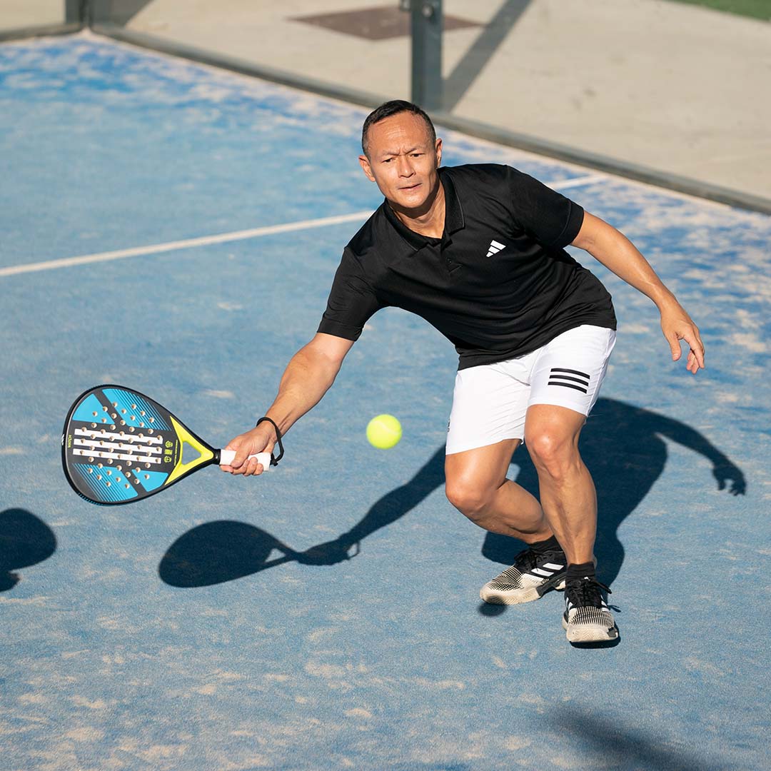 A man prepares to hit a ball with an Adidas racquet while playing padel