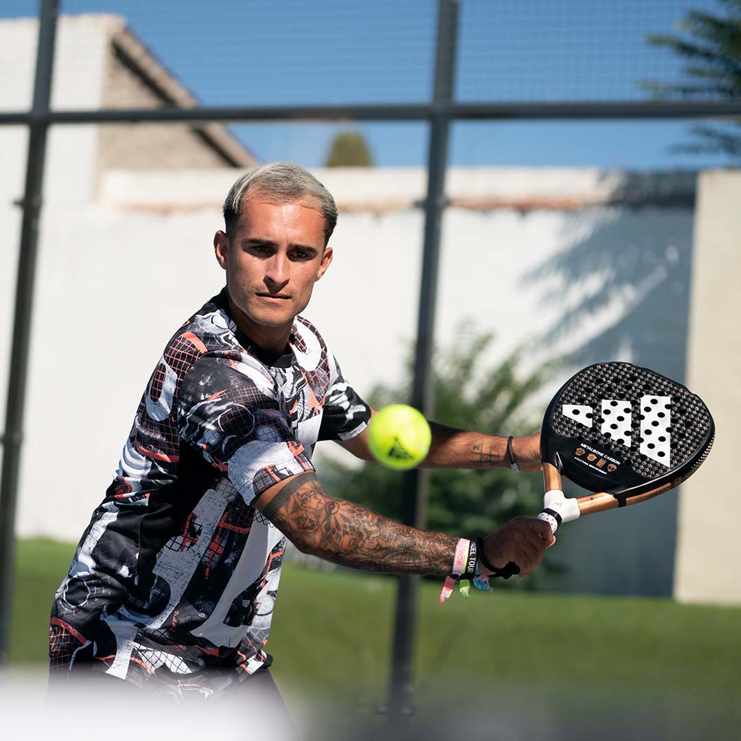 A man prepares to hit a ball with an Adidas racquet while playing padel
